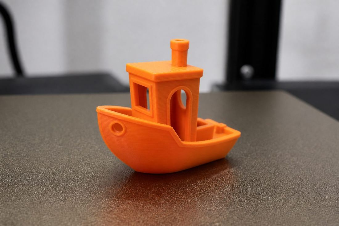 Barquito naranja de prueba 3D Benchy, de unos 4 cm, sobre la cama de la impresora